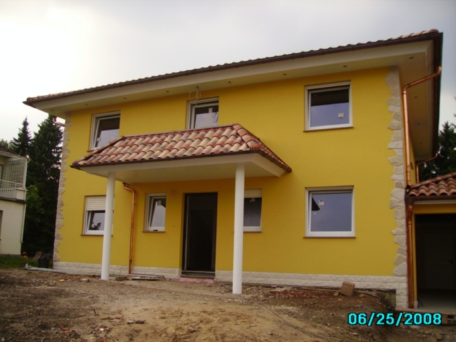 Gelbes, zweistöckiges Haus mit braunem Ziegeldach und weißen Fensterrahmen. Im unteren rechten Bereich des Bildes ist das Datum "06/25/2008" eingeblendet.