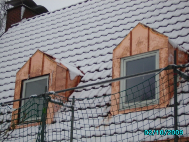 Schneebedecktes Ziegeldach mit zwei Kupfergauben. Im Vordergrund ein Schutznetz. Das Datum 02/10/2009 ist unten rechts zu sehen.